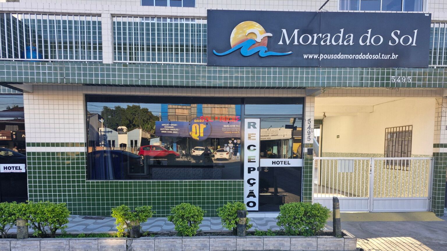 Fachada lateral do Hotel Morada do Sol com placas de identificação, janelas e vegetação.