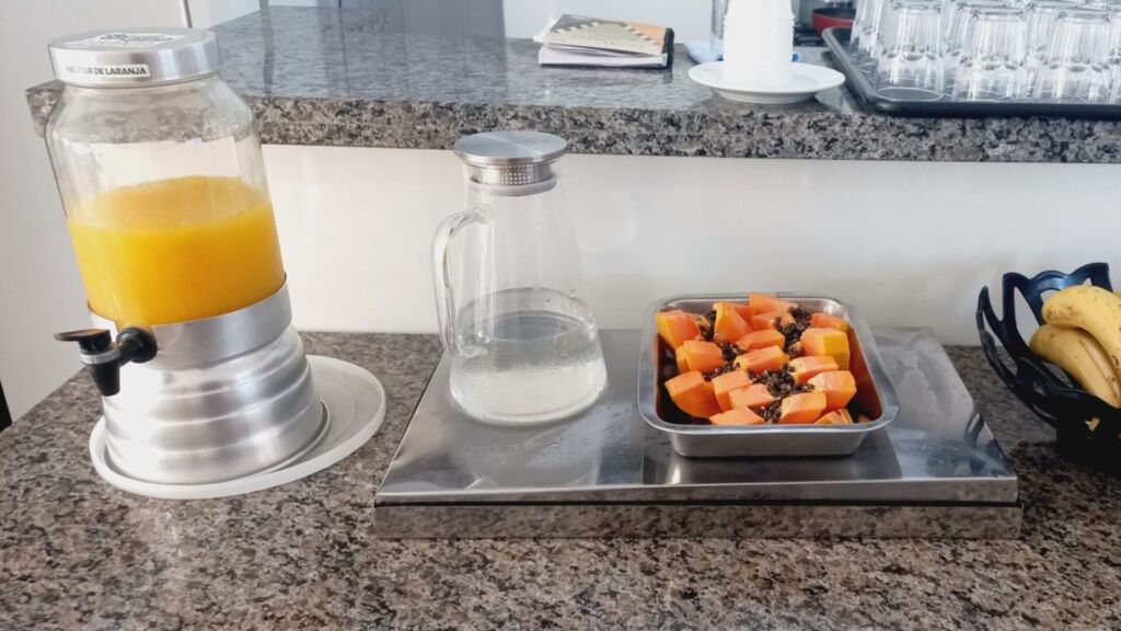 Balcão de granito com jarra de suco, jarra de água, frutas e copos organizados.