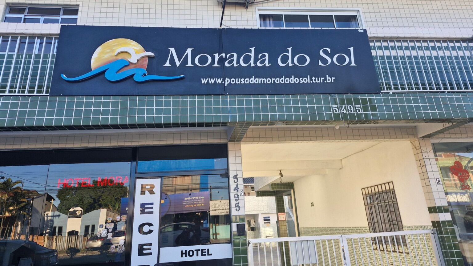Fachada lateral do Hotel Morada do Sol com placas de identificação, janelas e vegetação.