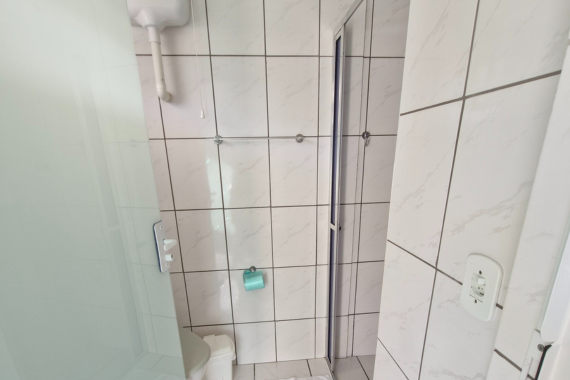 Banheiro com box de vidro e revestimento em azulejo branco.