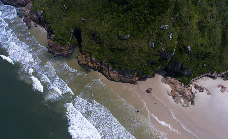 Vista aérea da Gruta das Encantadas e da encosta verde à beira-mar em Ilha do Mel, Paraná.