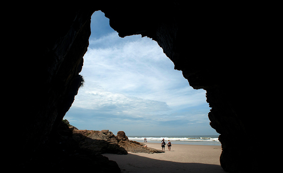 Vista do mar e da praia através da abertura escura da Gruta das Encantadas, em Ilha do Mel, Paraná.