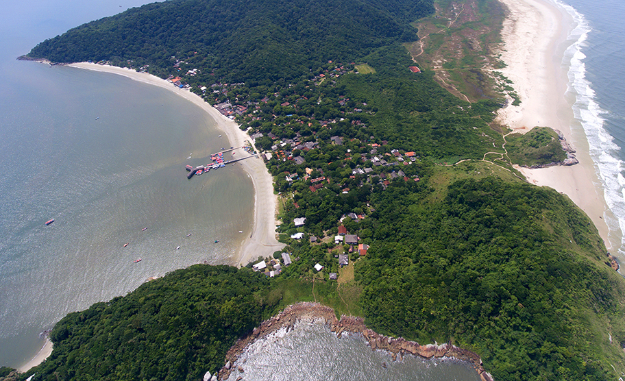 Vista aérea da Praia das Encantadas, com mar calmo, areia clara e vegetação ao fundo.