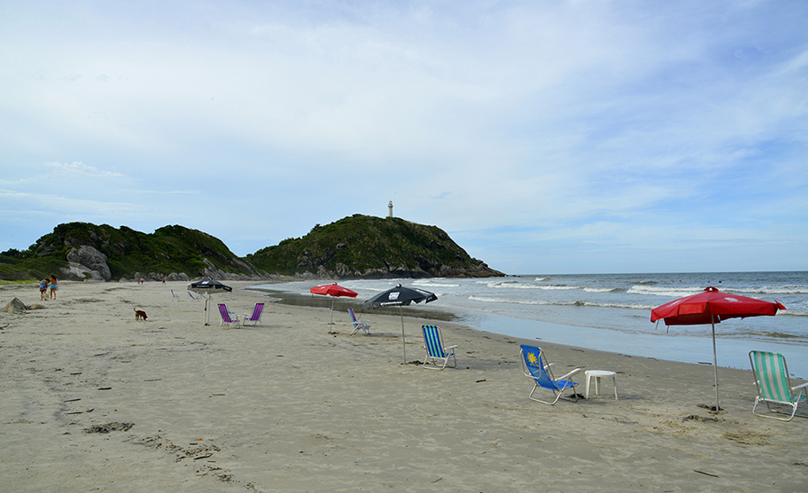 Praia com guarda-sóis e vista para o Morro do Farol, na Ilha do Mel, Paraná.